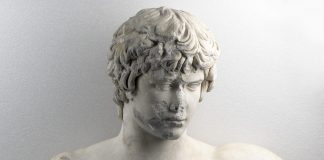 Γυμνή προτομή με κεφαλή του Αντίνοου. Βρέθηκε στην Πάτρα το 1856. Χρονολογείται λίγο μετά το 130 μ.Χ. Αρ. ευρ. Γ 418.